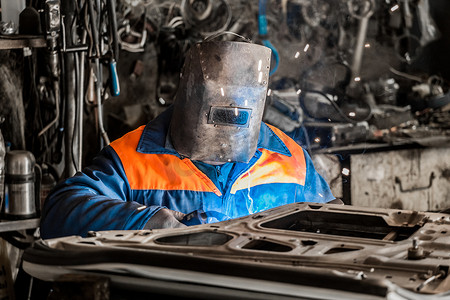 防护罩中的焊工在工业企业车间从事汽车门的焊接工作和修理