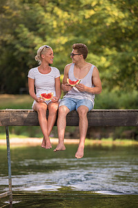 吃女孩西瓜摄影照片_一对夫妇坐在木桥上享用西瓜