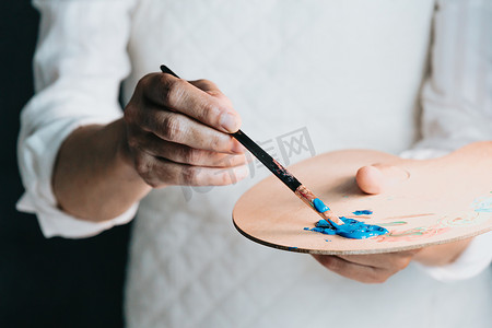 一位老妇人用蓝色颜料在画布上绘画的工作室图像。