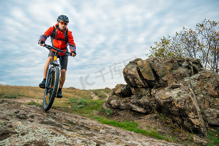 双人骑行山地车摄影照片_红色的骑自行车者在秋天的岩石小道上骑自行车。