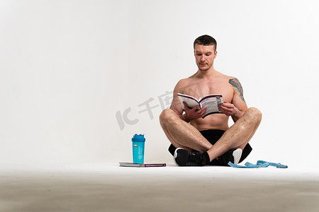 健美运动员在白色背景上阅读这本书，他的手被隔离在他的头底部，手上年轻肌肉发达，肌肉健身的人身体肌肉，欧洲运动。