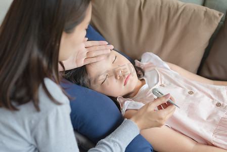 亚洲母亲用温度计检查孩子的体温，孩子在家发烧并生病了。