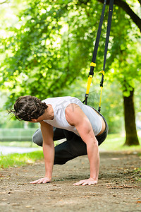 弹力带运动摄影照片_城市公园里的男人做悬挂训练器运动