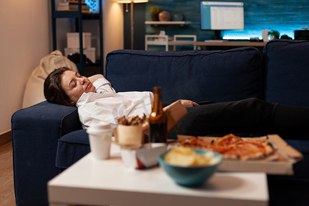 电视前的大型快餐外卖晚餐后，疲惫的女人在沙发上睡着了