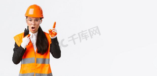 表情严肃的亚洲女工业工程师、安全帽技术员和带对讲机的统一指挥施工队，用无线电话解释或责骂某人