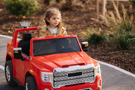 可爱的小女孩骑着红色电动吉普车在迷你城市里行驶。