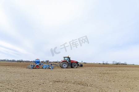 配备蓝色设备的红色拖拉机利用 GPS 导航在田间播种谷物，实现精准农业。