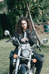 一个年轻的长发男子的肖像，一个穿着皮夹克的老骑自行车的人，骑着复古自行车，老式经典摩托车。