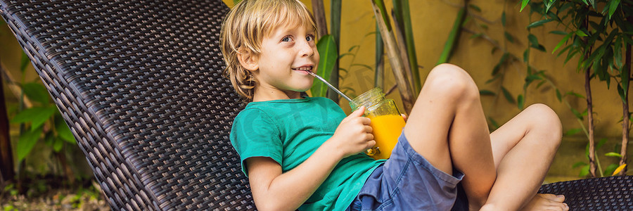 男孩在玻璃梅森罐子里喝着多汁的芒果冰沙，水池背景上有钢吸管。