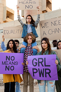 抗议者摄影照片_坐在男人肩膀上的年轻女抗议者在示威中举着“绝不不”的标语。