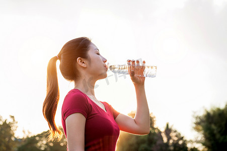 运动型女人在阳光下喝水。