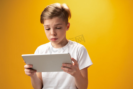 平板游戏摄影照片_黄色背景下玩数字平板电脑的小男孩