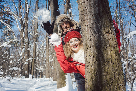 躲在树后摄影照片_冬天，女人和男人躲在树后扔雪球