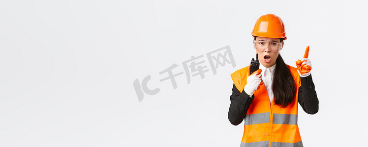 表情严肃的亚洲女工业工程师、安全帽技术员和带对讲机的统一指挥施工队，用无线电话解释或责骂某人