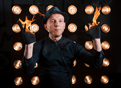 身穿黑帽、衬衫和光芒的专业魔术师玩火