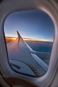 充满活力的日落期间，飞机机翼透过窗户