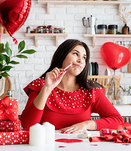 气球情书摄影照片_身穿红裙的年轻浪漫女人坐在装饰精美的厨房里写情书