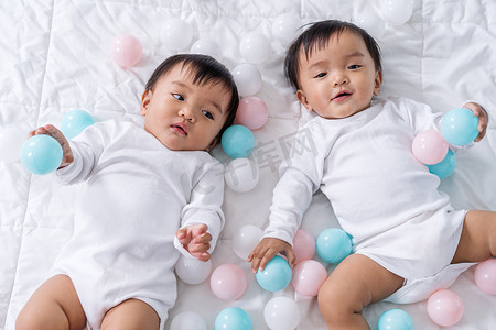 快乐的双胞胎婴儿在床上玩彩球