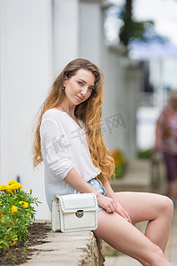 一个带着女士白色手提包的年轻女孩蹲在栏杆上，看着框架