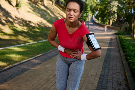 女跑步者在城市公园跑步时感到疲惫、侧抽筋、胃痛。