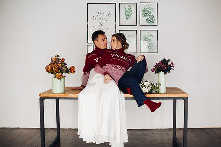 浪漫的情侣穿着红色毛衣，桌上写着家庭词，花瓶里插着鲜花。