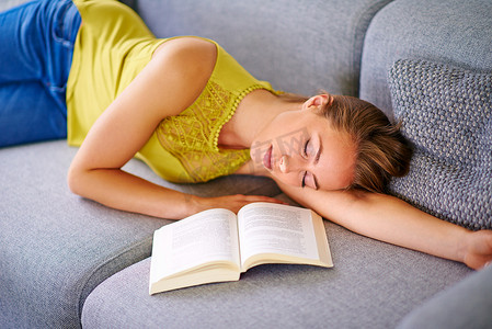 没有比家更放松的地方了……照片中一位年轻女子睡在家里沙发上的一本书旁。