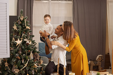 儿子给父亲摄影照片_幸福的年轻家庭，带着小儿子纳比圣诞树