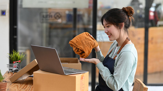 年轻女性小企业主在笔记本电脑上在线直播时展示衣服的照片