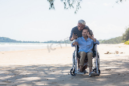 使用者摄影照片_坐在轮椅上的老妇人和丈夫是一位轮椅使用者，智能手机在海滩上自拍