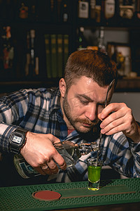 调酒师将龙舌兰酒沿着酒吧勺子的螺旋茎倒入带有香蕉利口酒的玻璃杯中
