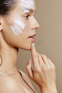 米色磨砂背景摄影照片_美丽的女人面膜霜清洁皮肤面部磨砂米色背景