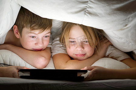 孩子们晚上在毯子下用平板电脑玩游戏，孩子们在平板电脑上看视频。