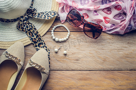 鞋子配饰摄影照片_十几岁女孩度假的配饰、帽子、时尚的夏季太阳镜、鞋子和木地板上的服装。