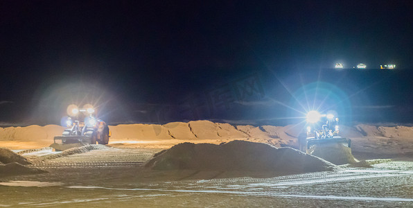 两名地勤人员晚上在海滩上用推土机搬运沙子