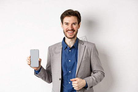 身穿西装的英俊微笑推销员展示空的智能手机屏幕，展示一个应用程序，站在白色背景上