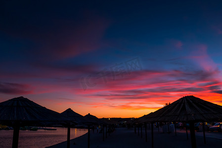 夕阳海摄影照片_美丽的蓝色和紫色日落、天空和稻草海滩伞的景色