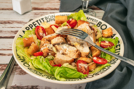精致的凯撒沙拉，配上鸡肉薄片、樱桃番茄和美味的蒜泥蛋黄酱，放在质朴的桌子上的小碗里。
