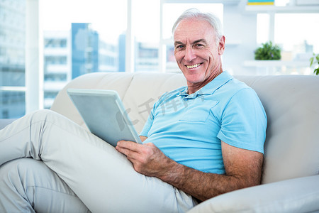 快乐的老人坐在沙发上，手里拿着数字平板电脑