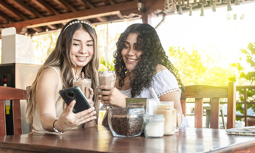 女朋友们摄影照片_两个女孩自拍喝咖啡，两个女朋友在咖啡店里拿着手机