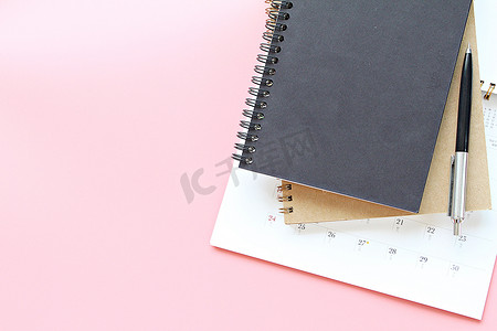 粉红色背景上的笔记本、日历和钢笔的顶视图或平躺