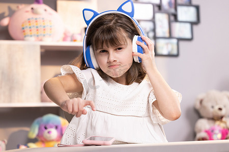 戴耳机的小女孩在智能手机上使用有趣的编辑应用程序，在社交网络中享受酷视频或音乐内容，玩在线游戏，远程交流