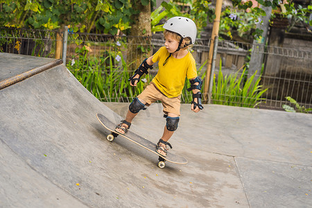 戴着头盔和护膝的运动男孩在滑板公园学习滑板。