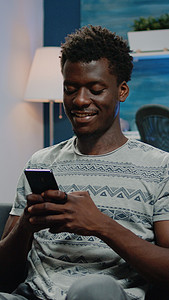 黑色沙发摄影照片_非洲裔美国人微笑着使用智能手机