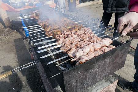 手串手串摄影照片_肉串在露天的烤架上煎炸，厨师的手可见