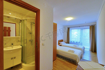 现代化装饰摄影照片_酒店的双人间配有铺有白色床罩的床和经过现代化装修的镜面浴室。