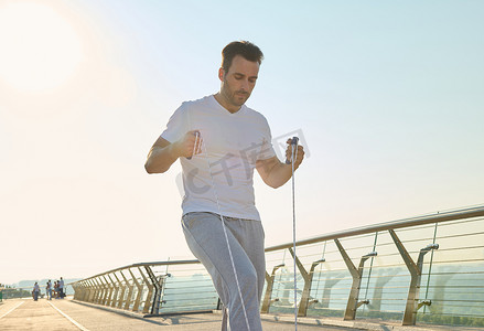 在美丽阳光明媚的夏日，英俊的中年运动员清晨在城市桥梁跑步机上进行跳绳训练。