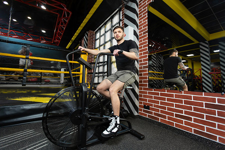 年轻的运动男拳击手在拳击场附近的健身自行车上训练