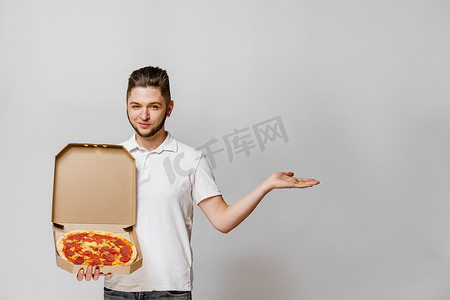 英俊的年轻快递员拿着披萨指向空的空间进行文字广告。