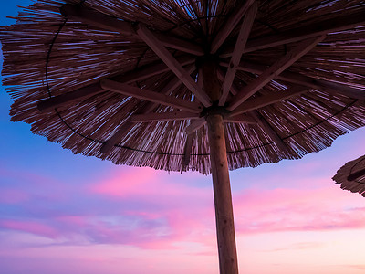 美丽的蓝色和紫色日落、天空和稻草沙滩伞的景色