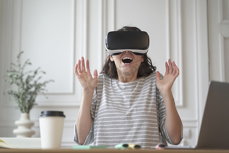 兴奋的企业家女士坐在家庭办公室戴着 VR 眼镜测试虚拟现实技术
